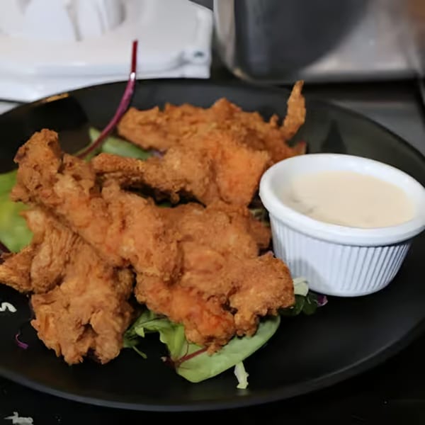 Crispy fried chicken tenders on a bed of greens with a side of dipping sauce at Cali's Sports Bar & Kitchen.