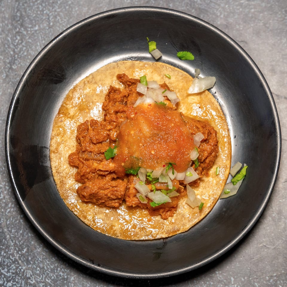 A single Cali's Sports Bar & Kitchen taco with red meat, salsa, and diced onions.