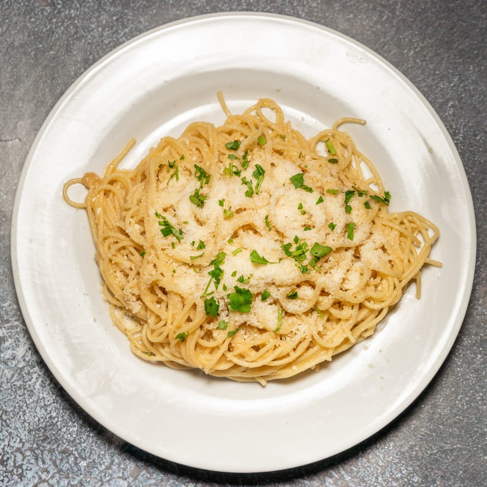 A white plate filled with spaghetti, topped with grated cheese and fresh parsley.