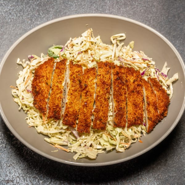 Crispy fried chicken cutlet, sliced and served over a bed of creamy coleslaw in a gray bowl.