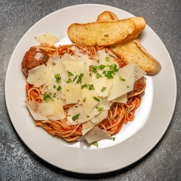 Spaghetti and meatballs with tomato sauce, topped with shaved Parmesan and parsley, served with garlic bread.