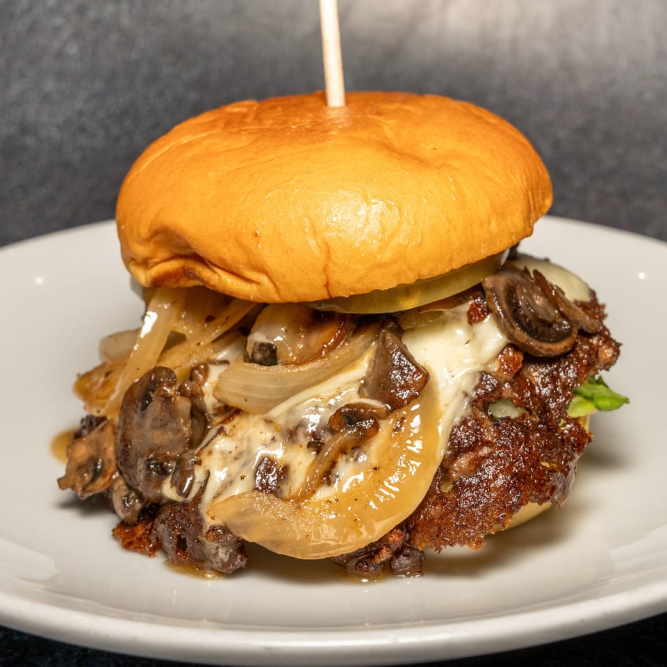 A Cali's Sports Bar & Kitchen burger with melted cheese, sautéed onions, and mushrooms on a white plate.