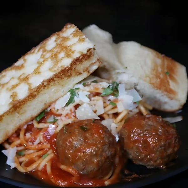 Spaghetti and meatballs with tomato sauce, parmesan, and two pieces of garlic bread.
