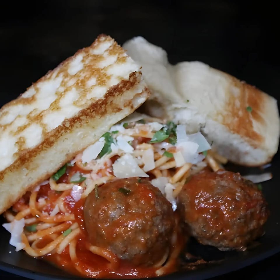 Spaghetti and meatballs with tomato sauce, parmesan, and two pieces of garlic bread.